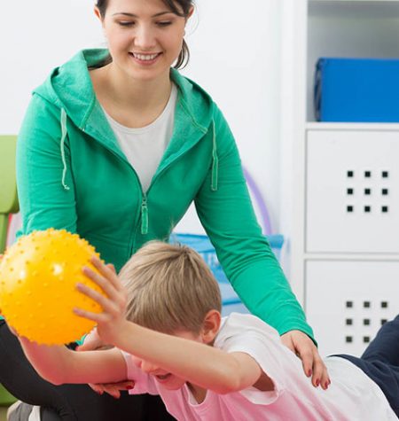 Boy exercising with small gym ball and his smiling instructor